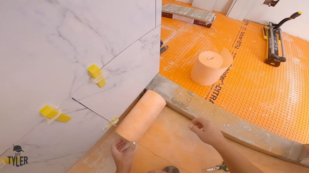 man applying Kerdi band for waterproofing walk-in shower curb