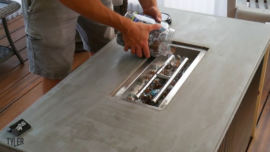 man adding fire glass to fire pan on top of  DIY deck fire table