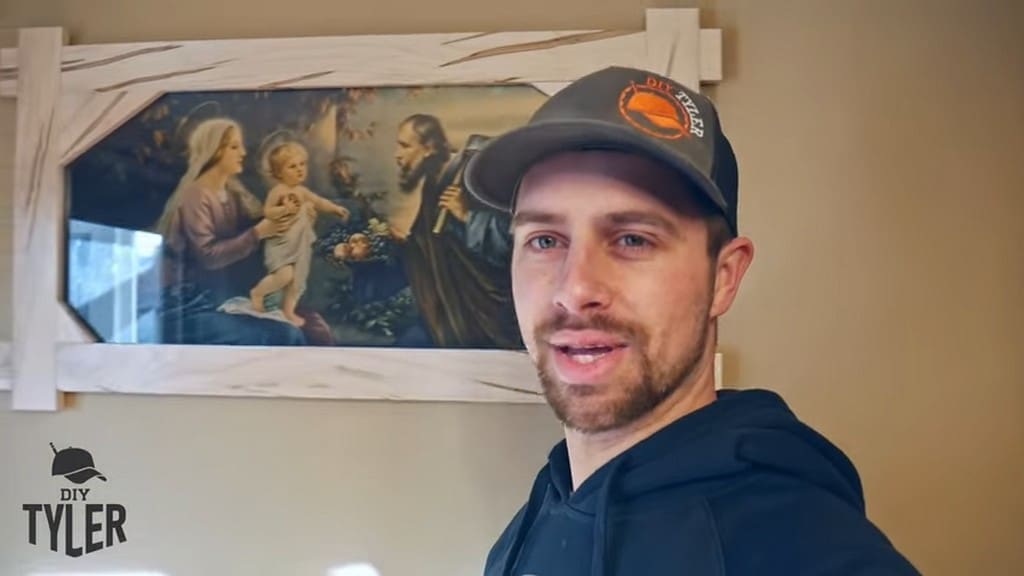 man standing in front of finished square picture frame with painting of Holy Family