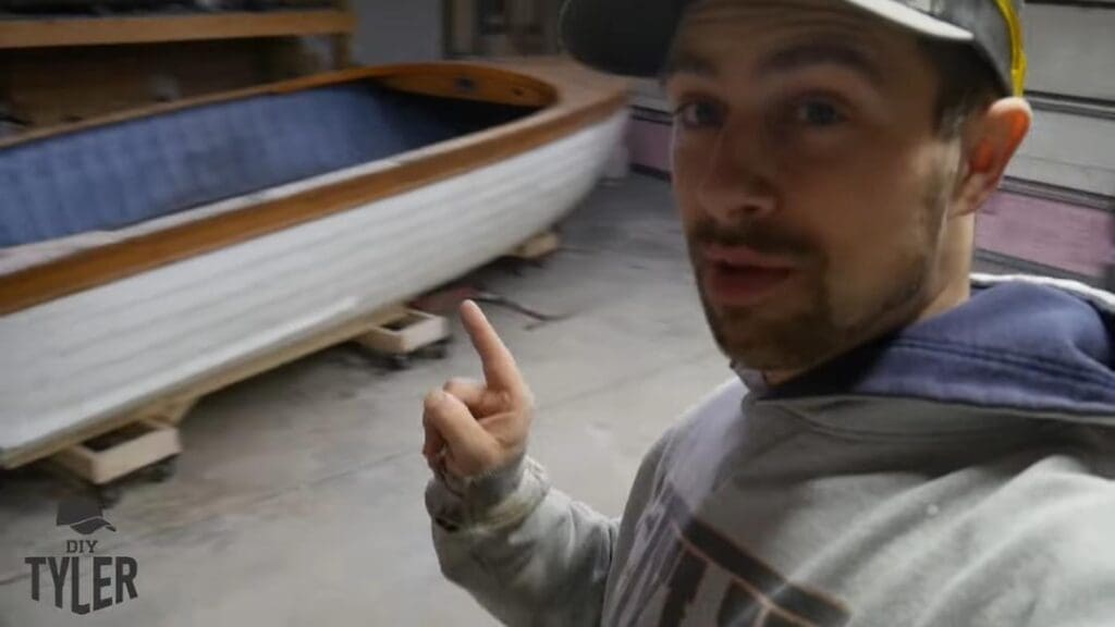 man gesturing to wooden boat in workshop
